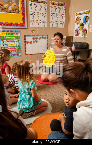 Holding a cutout of an Easter egg, a Hispanic teacher works with young children and their parents at a 'Learning Link' classroom in Tustin, CA, conducting a workshop in interactive behavior. Using specially designed activities, the class teaches parents how to engage their children in meaningful play. Stock Photo