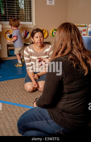 A Hispanic teacher advises a mother as her son plays at a "Learning Link" classroom in Tustin, CA, conducting a workshop in interactive behavior. Using specially designed activities, the class teaches parents how to engage their children in meaningful play. Stock Photo