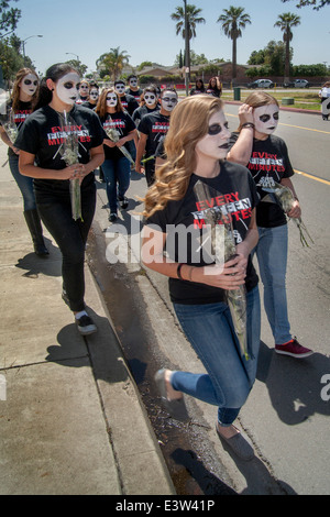 Dressed in 'Grim Reaper' costumes and carrying memorial flowers, high school students participate in a dramatization of an auto accident caused by drunk driving for the education of schoolmates in Anaheim, CA. Note grotesque makeup and 'Every Fifteen Minutes' t shirts supplied by the organization sponsoring the event. Stock Photo