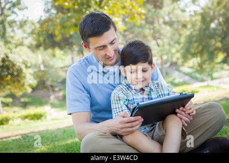Handsome Mixed Race Father and Son Playing on a Computer Tablet Outside. Stock Photo