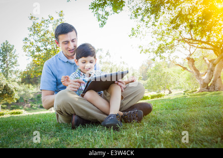 Handsome Mixed Race Father and Son Playing on a Computer Tablet Outside. Stock Photo