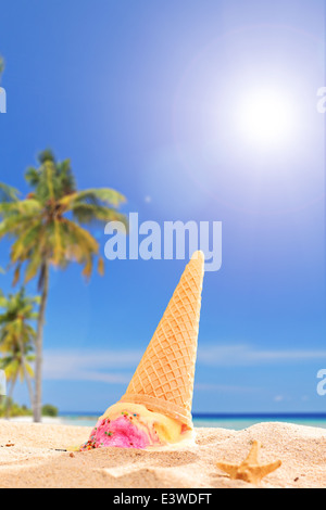 An ice cream melting in the sand on a tropical beach on sunny day Stock Photo