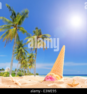 Ice cream thrown in the sand on a tropical beach with the focus on the ice cream Stock Photo