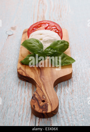 Basil leaf, mozzarella cheese and tomato slice on cutting board Stock Photo