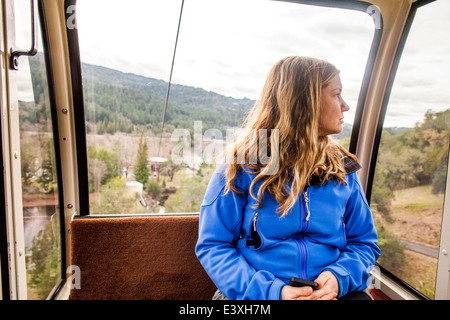 Caucasian woman riding in aerial tram Stock Photo