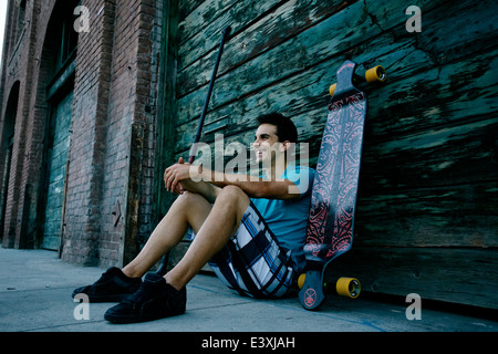 Caucasian man sitting with skateboard and land paddle Stock Photo