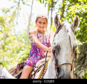 Mixed race girl riding horse in jungle