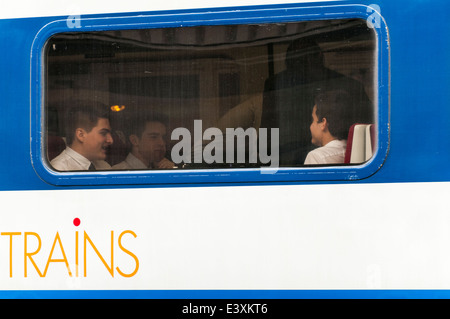 Looking into a railway carriage window at 3 passengers wearing white shirts travelling together sitting at a table Stock Photo