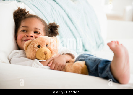Black girl hugging teddy bear on sofa Stock Photo