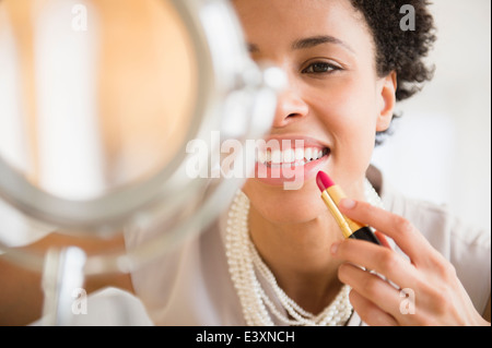 Black woman applying makeup in mirror Stock Photo