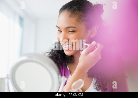 Mixed race woman applying makeup in mirror Stock Photo