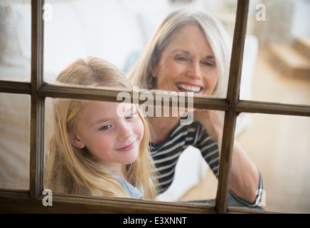 Senior Caucasian woman and granddaughter looking out window Stock Photo