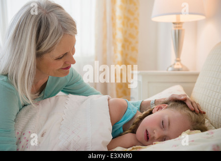 Senior Caucasian woman putting granddaughter to bed Stock Photo