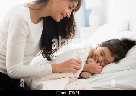 Hispanic mother tucking daughter into bed Stock Photo