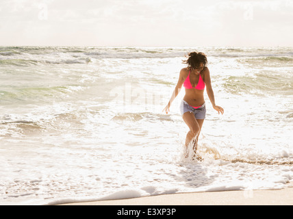 African American woman playing in waves on beach Stock Photo