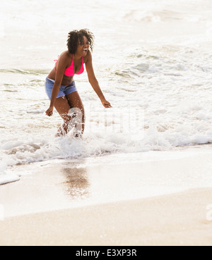 African American woman playing in waves on beach Stock Photo