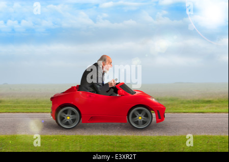 senior man in a suit driving a toy racing car Stock Photo