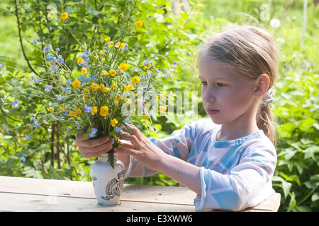 little girl putting bunch of summer wild flowers to the old vase on wooden table Stock Photo