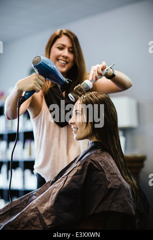 Stylist blow drying client's hair in salon Stock Photo