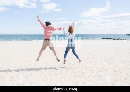Rear view of couple jumping mid air on beach Stock Photo