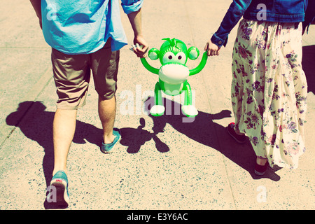 Cropped rear view of couple holding hands with inflatable monkey Stock Photo