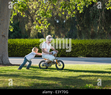 Three year old boy pushing grandmother on cycle in park Stock Photo