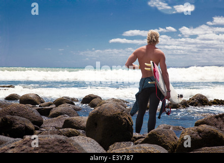 Young adult male surfer watching sea from beach rocks