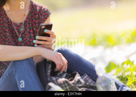 Cropped shot of young woman sitting in park with smartphone Stock Photo