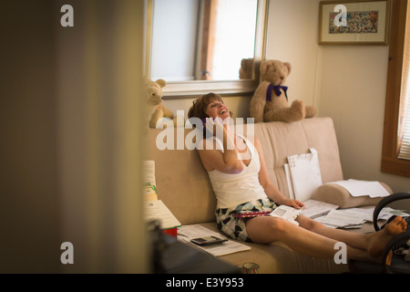 Mid adult woman sitting on sofa, using mobile phone Stock Photo