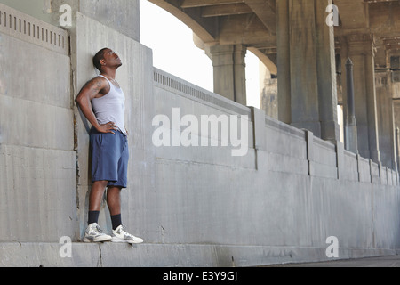 Exhausted young male runner leaning against city bridge Stock Photo