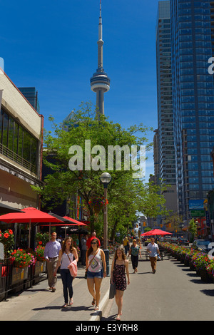 Pedestrians walking on John Street Toronto with cafes and CN tower and highrise condos Stock Photo