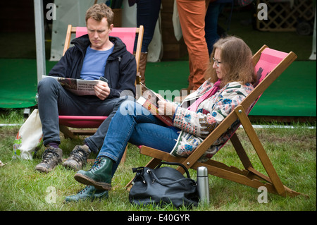 Man and woman sitting in deckchairs reading newspapers outdoors at Hay Festival 2014 ©Jeff Morgan Stock Photo