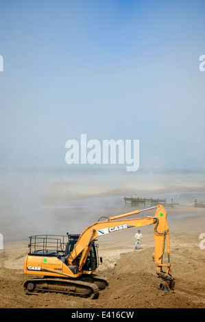 Excavator digging out sand on beach in a sea mist Stock Photo - Alamy