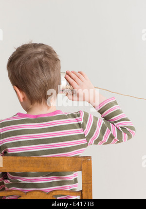 Little child listening with tin can phone. Conceptual image of childhood play and communication. Stock Photo