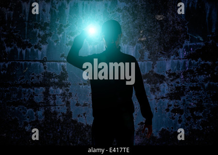 Shadow of man in front of grungy wall holding a torch light at night Stock Photo
