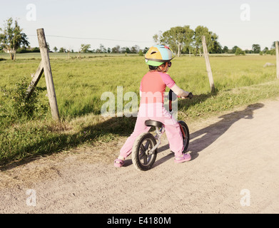 Tranquil summer landscape. Little girl riding a bike on a rural road in Sweden. Stock Photo