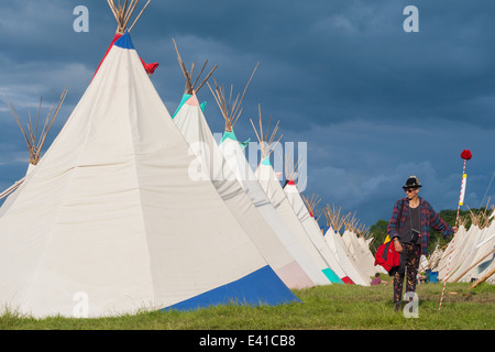 GLASTONBURY, UK - JUNE 28: A festival goers stands by a row of tipi tents at Glastonbury Festival on 28th June, 2014 Stock Photo