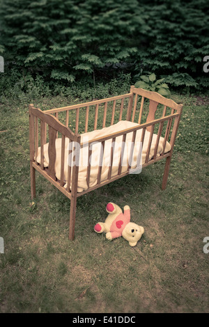 A teddy bear on the ground under a vintage old wooden crib out side in a yard. Stock Photo