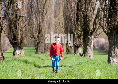 Twelve year old boy walking along tree lined field Stock Photo