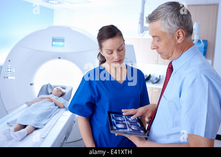 Girl in CT scanner, doctor and radiographer looking at scan on digital tablet Stock Photo