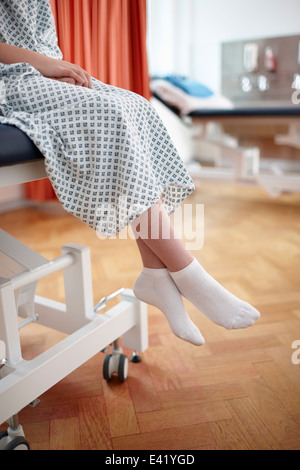 Girl sitting on hospital bed, wearing examination gown Stock Photo