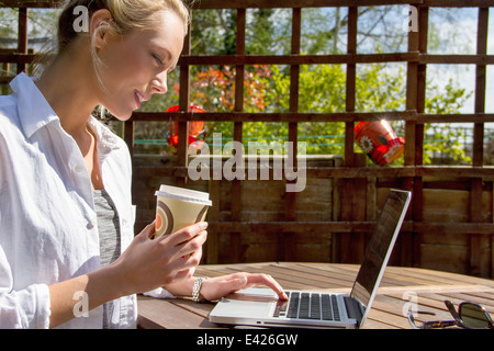 Young woman with takeaway coffee and laptop in garden Stock Photo