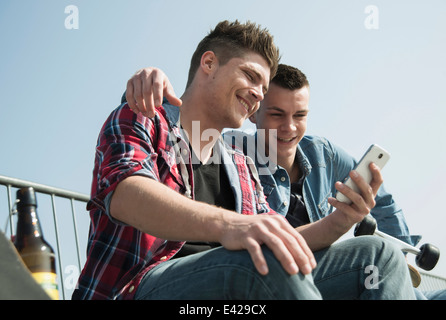 Young men in skatepark, using smartphone, drinking bottle of beer Stock Photo