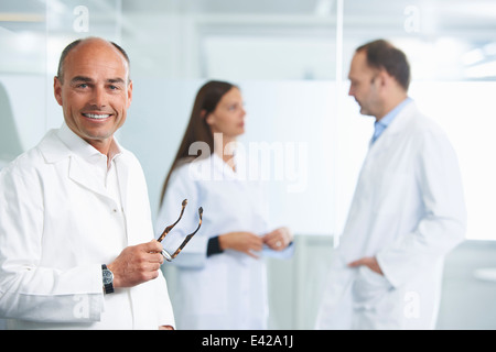 Male doctor by reflective wall, colleagues in background Stock Photo