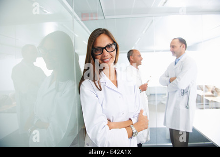 Female doctor by reflective wall, colleagues in background Stock Photo