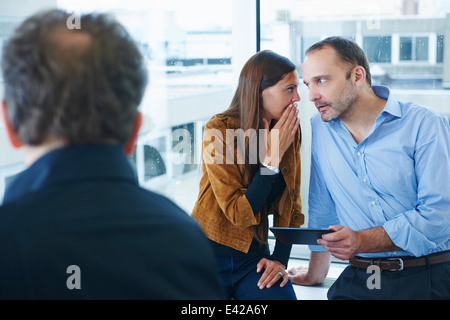 Businesswoman whispering to man in office Stock Photo