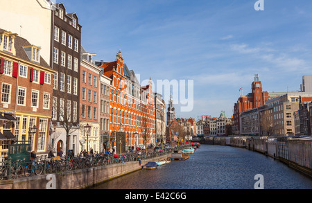 AMSTERDAM, NETHERLANDS - MARCH 19, 2014: Colorful houses facades on the canal in spring sunny day. Ordinary people are walking Stock Photo