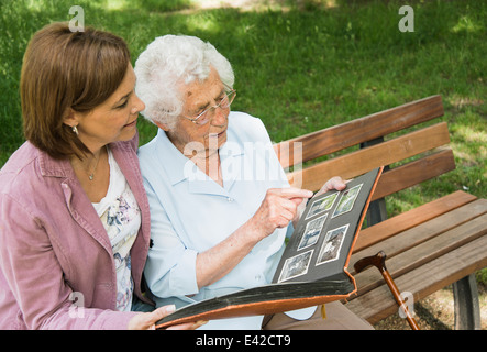 Senior woman sitting on park bench with granddaughter, looking at old photograph album Stock Photo