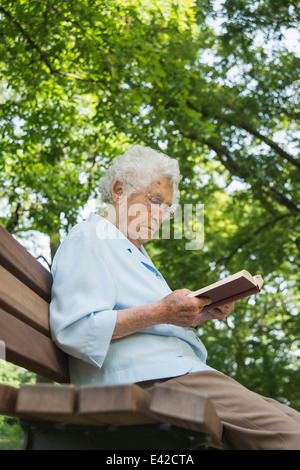 Senior woman sitting on park bench reading bible Stock Photo