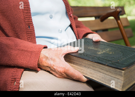 Mid section of senior woman, sitting on park bench, holding bible Stock Photo